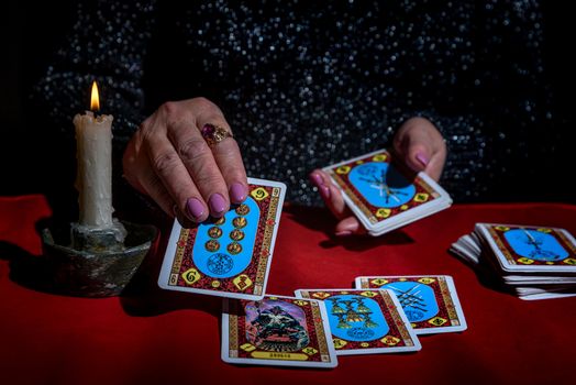 A woman reads Tarot cards by candlelight on a red table