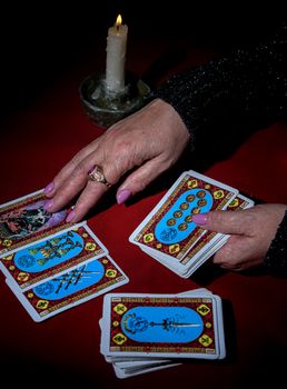 A woman reads Tarot cards by candlelight on a red table