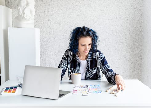 Designer working with colour palettes and laptop in her art studio