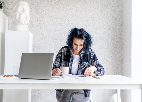 Designer working with colour palettes and laptop in her art studio