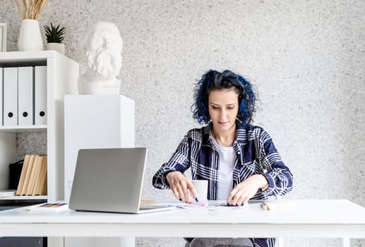 Designer working with colour palettes and laptop in her art studio