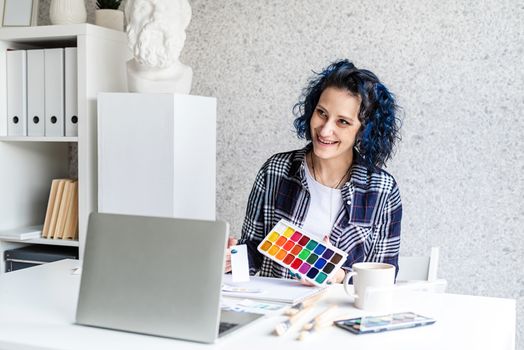 Designer working with colour palettes and laptop in her art studio