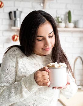 Christmas and New Year. Brunette woman holding a cup of marshmallow cocoa in the kitchen