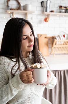 Christmas and New Year. Brunette woman holding a cup of marshmallow cocoa in the kitchen