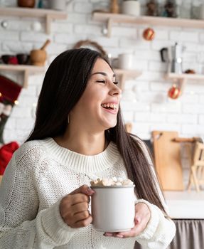 Christmas and New Year. Brunette woman holding a cup of marshmallow cocoa in the kitchen