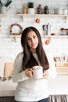 Christmas and New Year. Brunette woman holding a cup of marshmallow cocoa in the kitchen