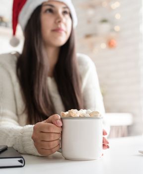 Christmas and New Year. Brunette woman in santa hat holding a cup of marshmallow cocoa