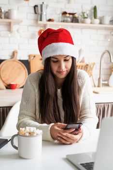 Christmas and New Year. Young brunette woman chatting with friends using her mobile phone at the kitchen