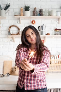 Christmas and New Year. Young smiling woman with a sparkler celebrating Christmas in the kitchen