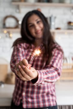 Christmas and New Year. Young smiling woman with a sparkler celebrating Christmas in the kitchen