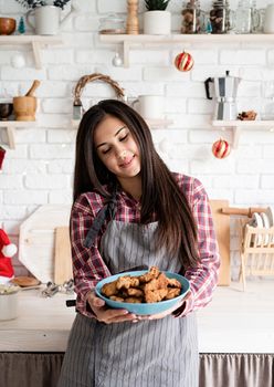 Cooking and baking. Young smiling woman in apron holding a plate with home baked cookies in the kitchen