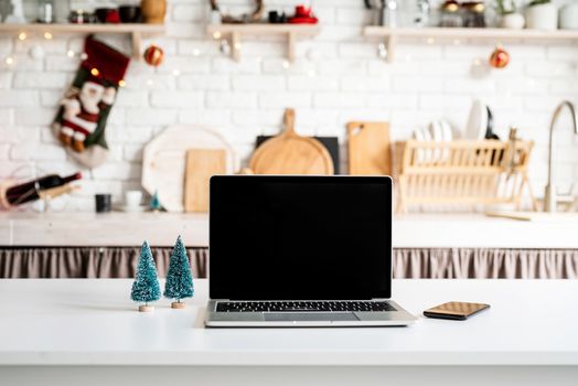 Interior light grey kitchen and red christmas decor. Laptop with black screen on festive kitchen in Christmas decorations, front view