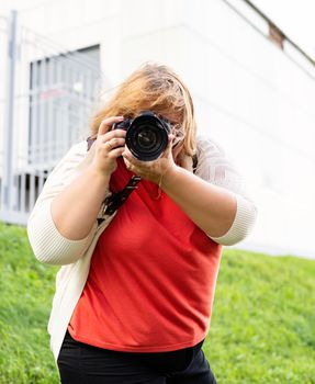 Body positive. Portrait of overweight woman taking pictures with a camera in the park