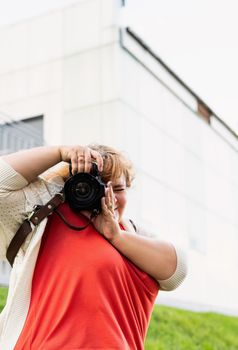 Body positive. Portrait of overweight woman taking pictures with a camera in the park