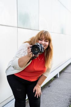 Body positive. Portrait of overweight woman taking pictures with a camera outdoors