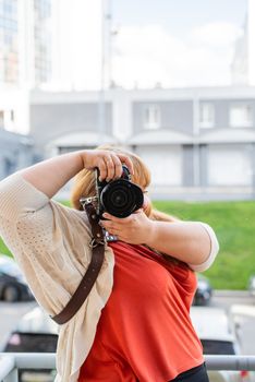 Body positive. Portrait of overweight woman taking pictures with a camera outdoors