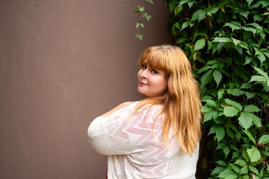 Body positive. Confident overweight woman posing on the brown solid wall on the street