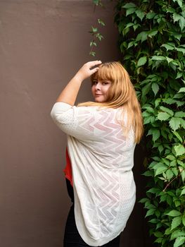 Body positive. Confident overweight woman posing on the brown solid wall on the street