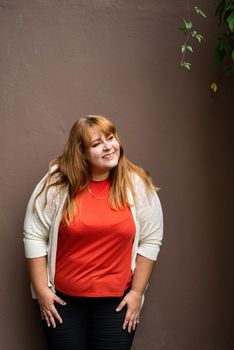 Body positive. Confident overweight woman posing on the brown solid wall on the street