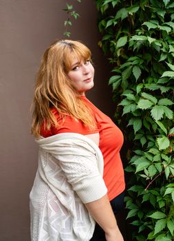 Body positive. Confident overweight woman posing on the brown solid wall on the street