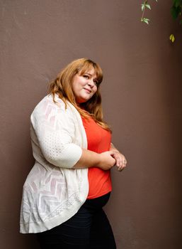 Body positive. Confident overweight woman posing on the brown solid wall on the street