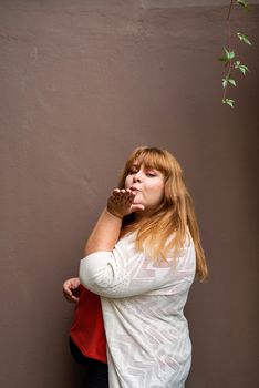 Body positive. Confident overweight woman posing on the brown solid wall on the street