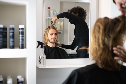 Handsome blonde male client getting haircut by black female hairdresser