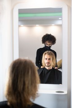 Handsome blonde male client getting haircut by black female hairdresser