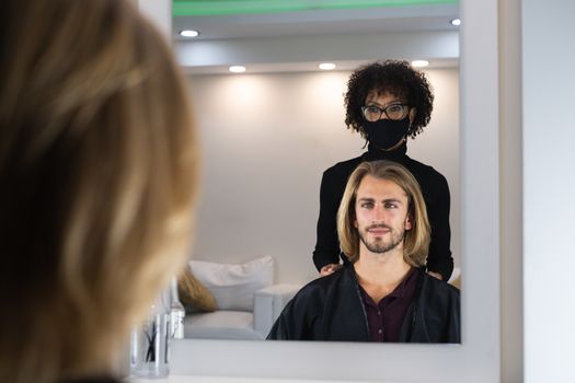 Handsome blonde male client getting haircut by black female hairdresser