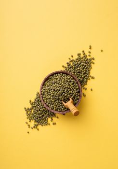 Mung beans top view on yellow background, minimal style. Wooden bowl with green mung beans and wooden spoon top view flat lay