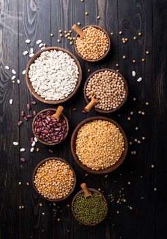 Various dried legumes in wooden bowls top view flat lay on black rustic background