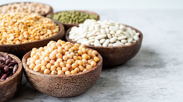 Various dried legumes in wooden bowls on wooden background