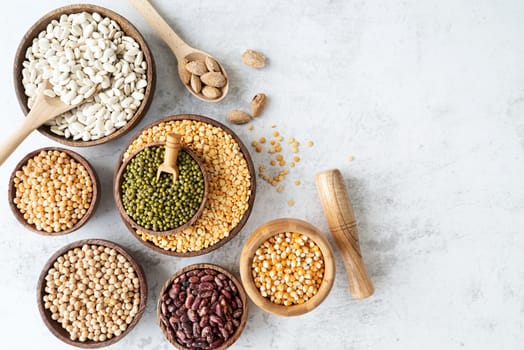 Various dried legumes in wooden bowls top view flat lay on white marble background