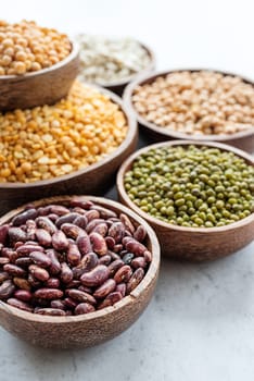 Various dried legumes in wooden bowls on white marble background with copy space