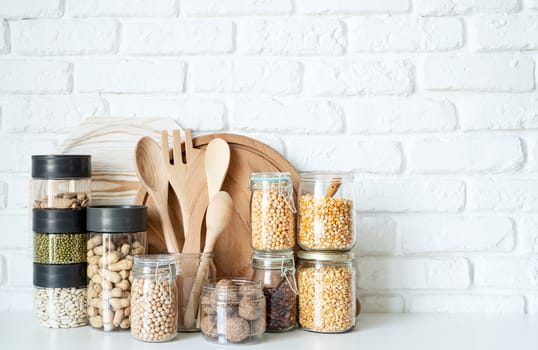 Various dried legumes in glass jars on white marble background with copy space in the kitchen