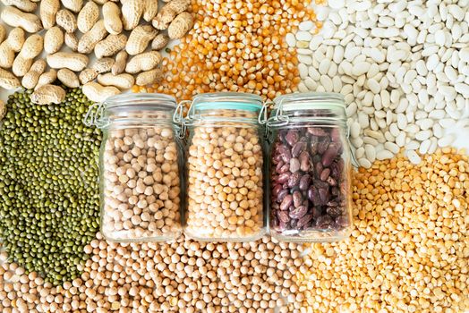 Various dried legumes in glass jars on white marble background top view flat lay