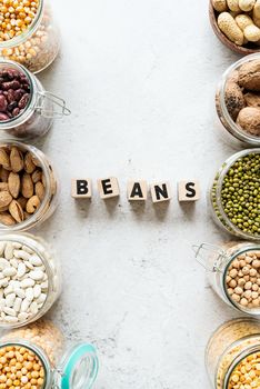 Various dried legumes in wooden bowls with the text Beans top view flat lay on white marble background