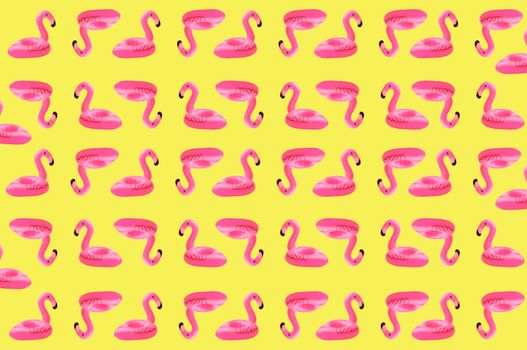 Creative concept of beach and summer vacation.Seamless pattern from inflatable pink mini flamingos on a sandy background.Floating inflatable flamingo. Flamingo Trend Inflatable Toy. Summer background