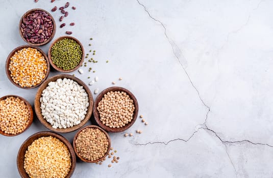 Various dried legumes in wooden bowls top view flat lay on gray rustic background with copy space