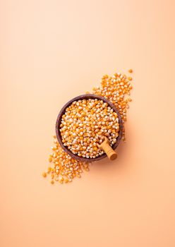 Corn top view on orange background, minimlal style. Wooden bowl with yellow corn and wooden spoon top view flat lay