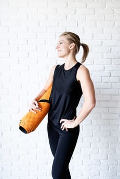 Healthy lifestyle. Sport and fitness. Smiling athletic woman in black sportwear on white brick wall background