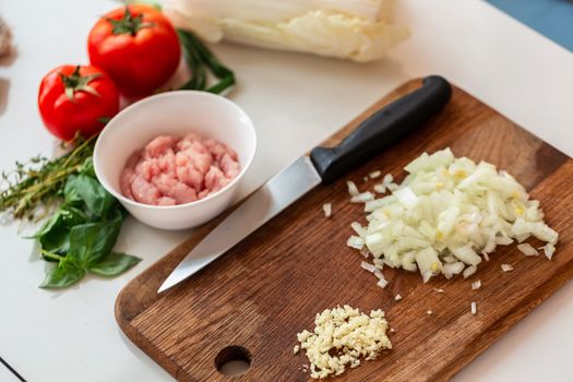 Cooking cabbage rolls with chicken mince at home. Slicing onions and garlic on the wooden board for the dish. How to cook cabbage rolls instructions.