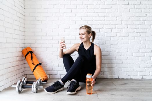 Healthy lifestyle. Sport and fitness. Young smiling fitness woman doing selfie after workout sitting at the floor drinking water