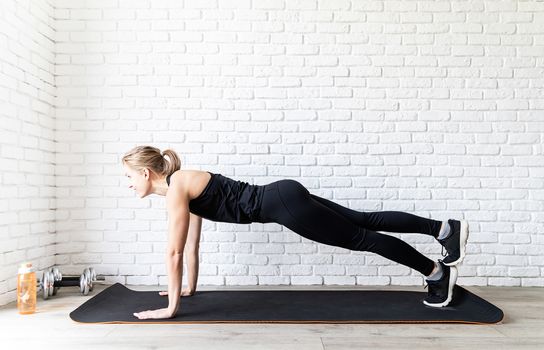 Healthy lifestyle. Sport and fitness. Young fit woman in black sportswear doing push ups at home