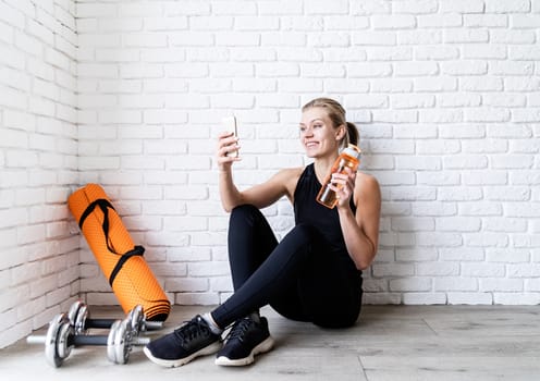 Healthy lifestyle. Sport and fitness. Young smiling fitness woman doing selfie after workout sitting at the floor drinking water