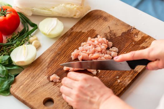 Cooking chicken tenders at home. Slicing chicken fillet into small pieces for the mince on the wooden board. How to cook cabbage rolls instructions.