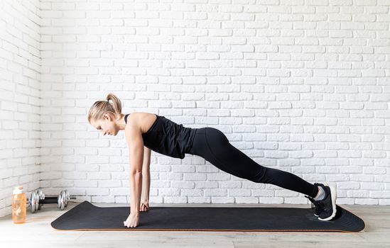 Healthy lifestyle. Sport and fitness. Young fit woman in black sportswear doing push ups at home