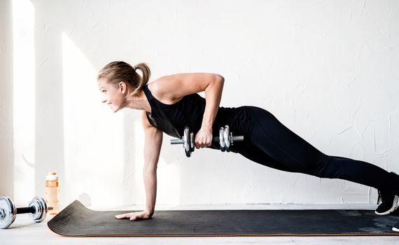 Healthy lifestyle. Sport and fitness. Young blond woman working out doing dumbbell lifts training her back and arms