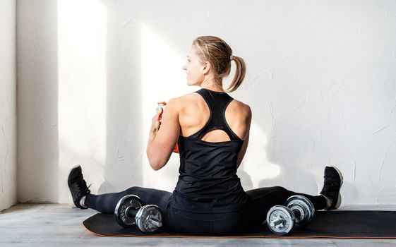 Healthy lifestyle. Sport and fitness. Rear view of young blond woman working out with dumbbells showing her back and arms muscles