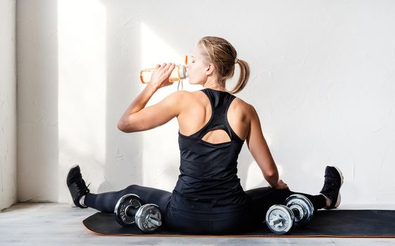 Healthy lifestyle. Sport and fitness. Rear view of young blond woman working out with dumbbells showing her back and arms muscles